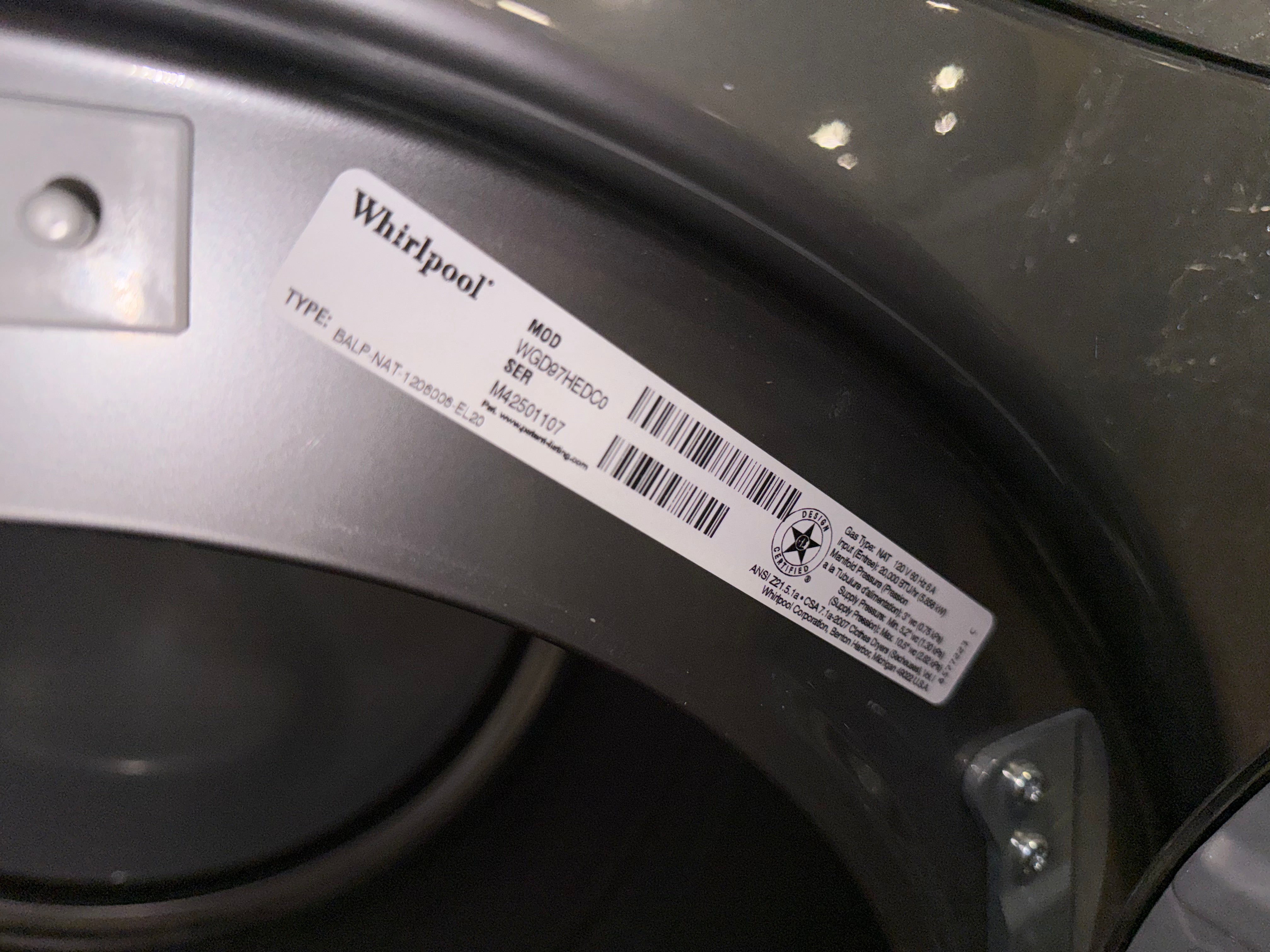 A close-up of a Whirlpool appliance label sticker on the inner silver and dark gray curved panel of a washing machine.