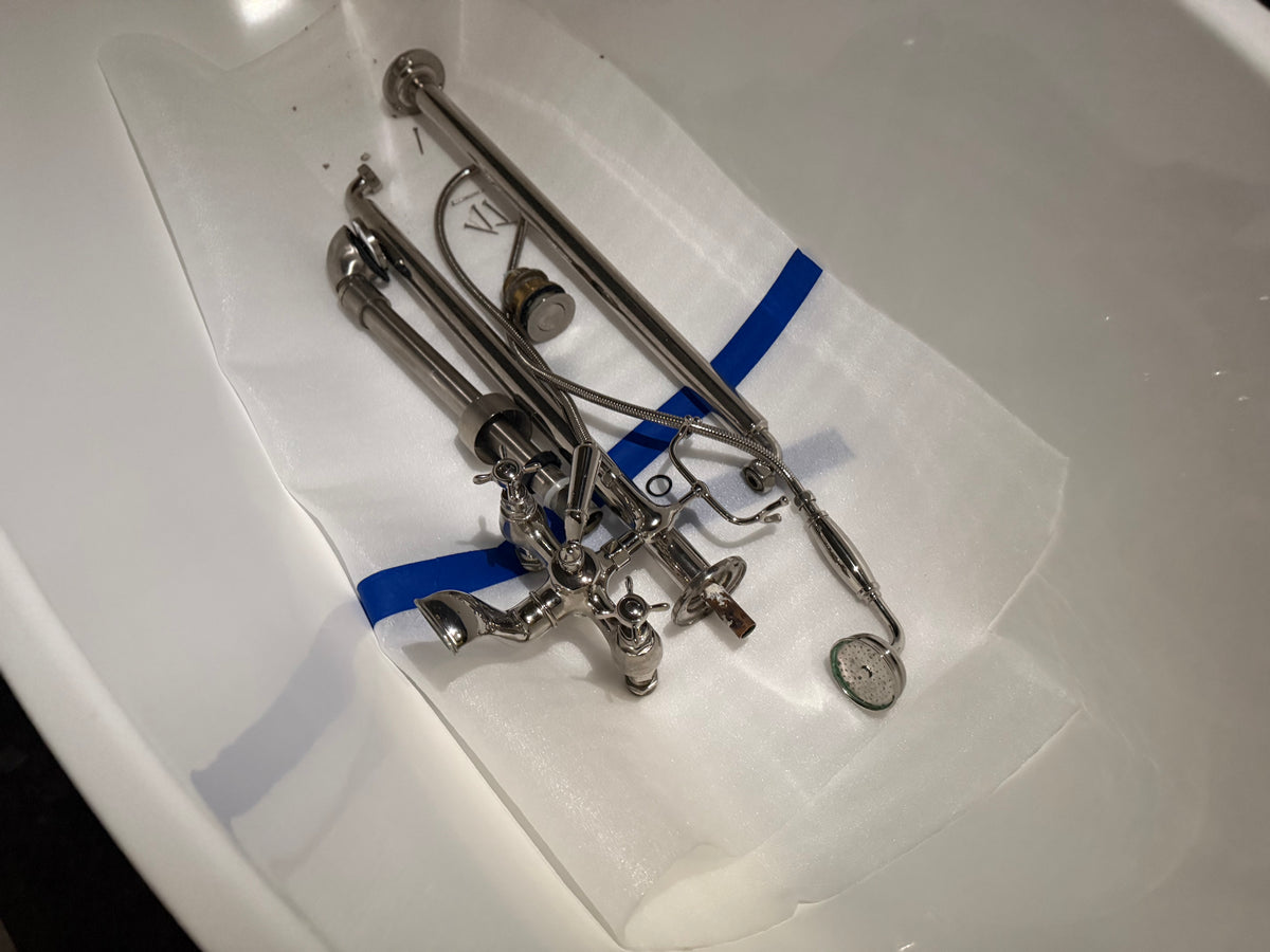 A set of polished silver metal faucet parts and fixtures laid out on a white protective sheet inside a white sink basin.