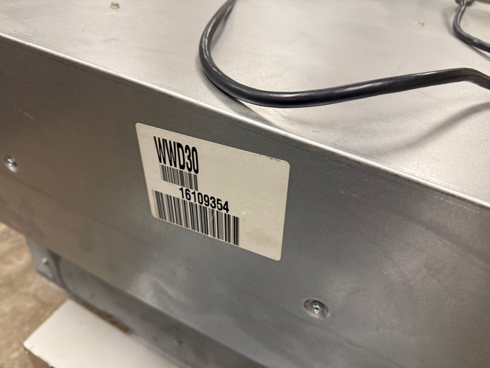 Close-up of the side of a metallic silver appliance or equipment unit with a white barcode label reading WVD30 and a black power cord.