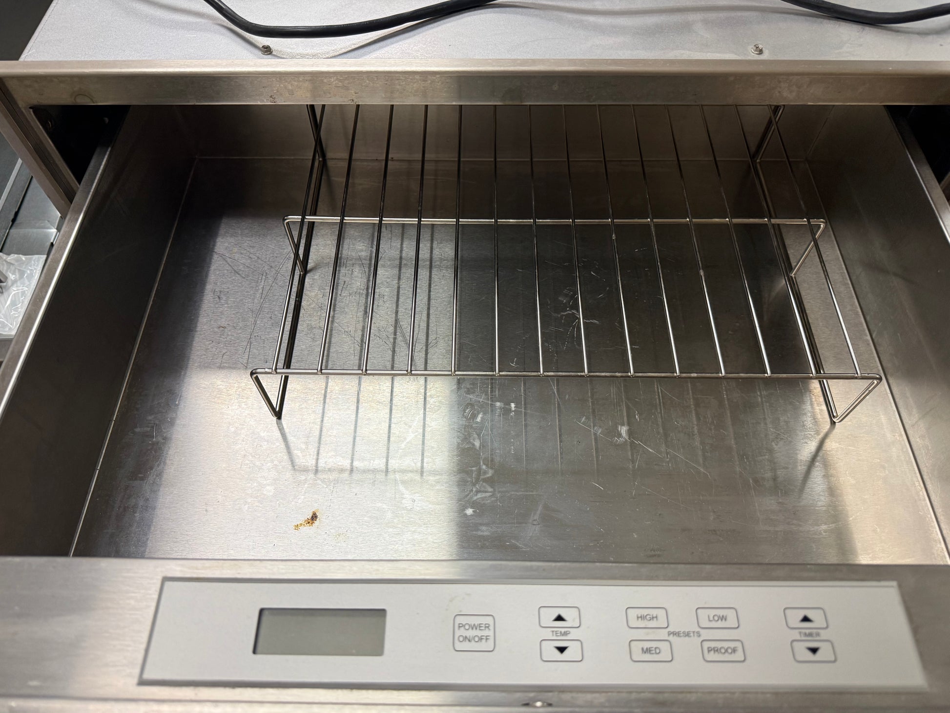 A stainless steel thermal circulator or heating bath with an open drawer-style front, showing a metal wire rack inside and a control panel with buttons at the bottom.