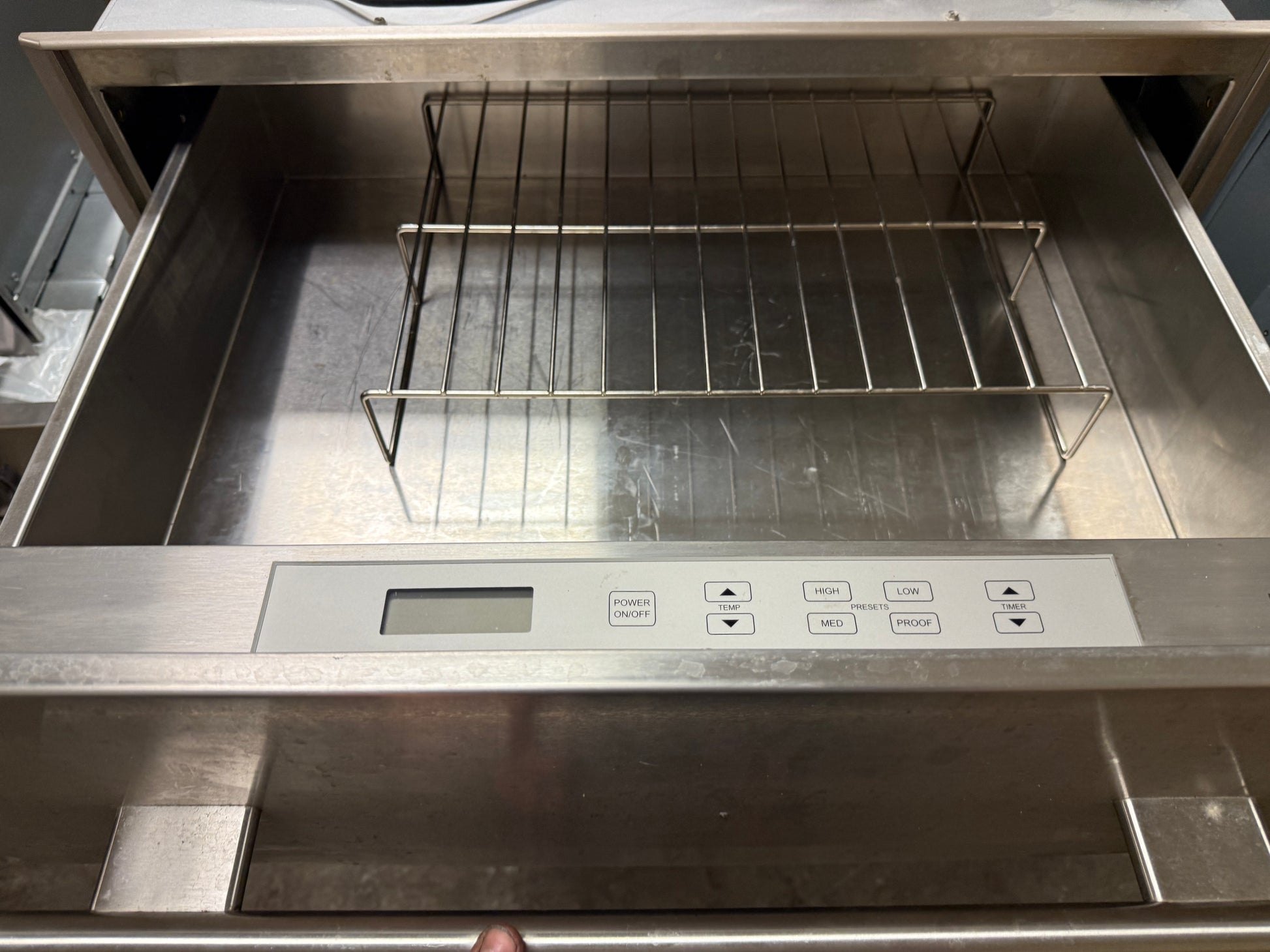 A stainless steel drawer-style oven or probe oven with a metal wire rack inside and a front control panel showing temperature and time settings.