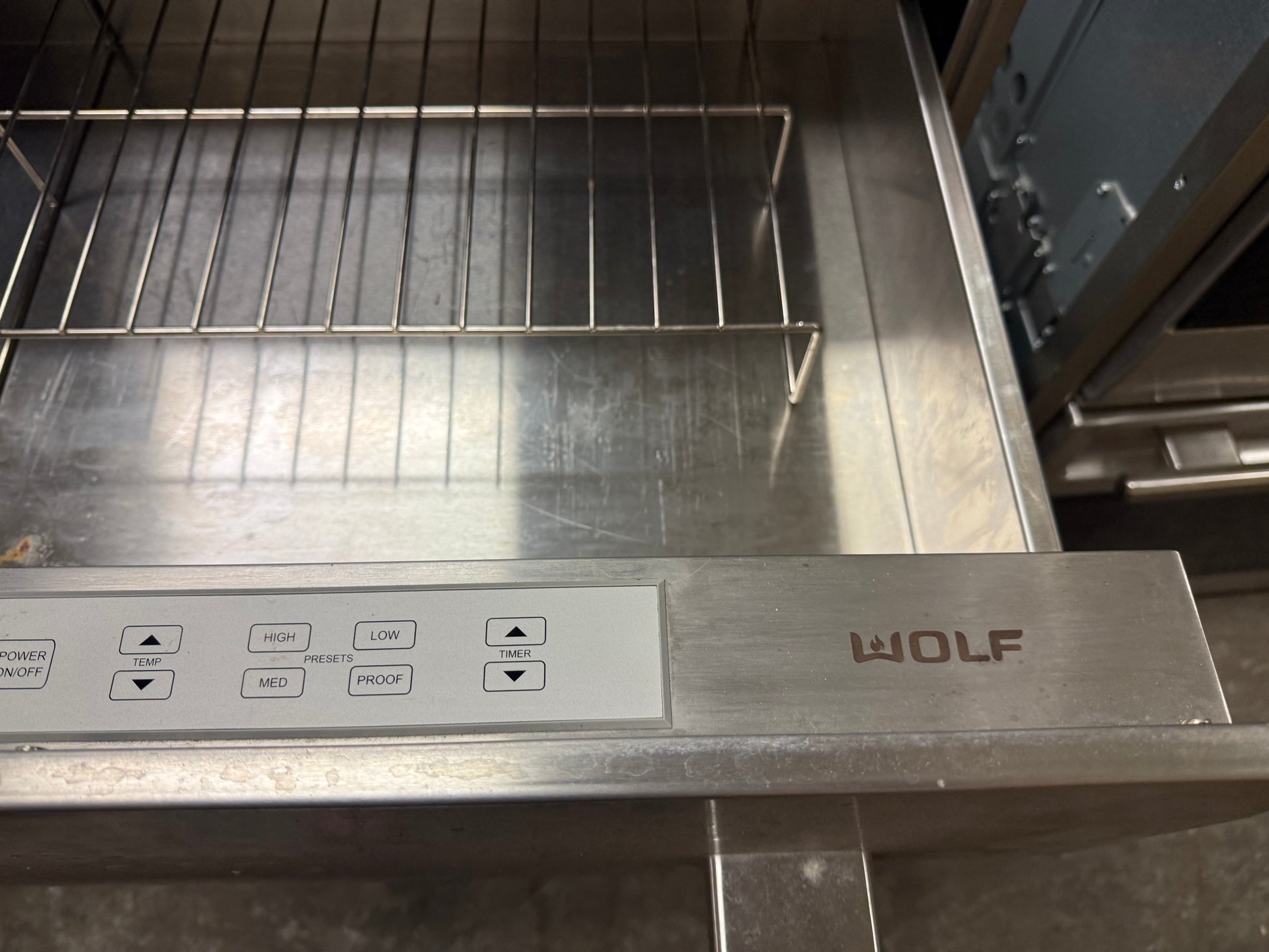 Close-up of a stainless steel Wolf oven interior with a metal rack and a control panel featuring the WOLF logo.