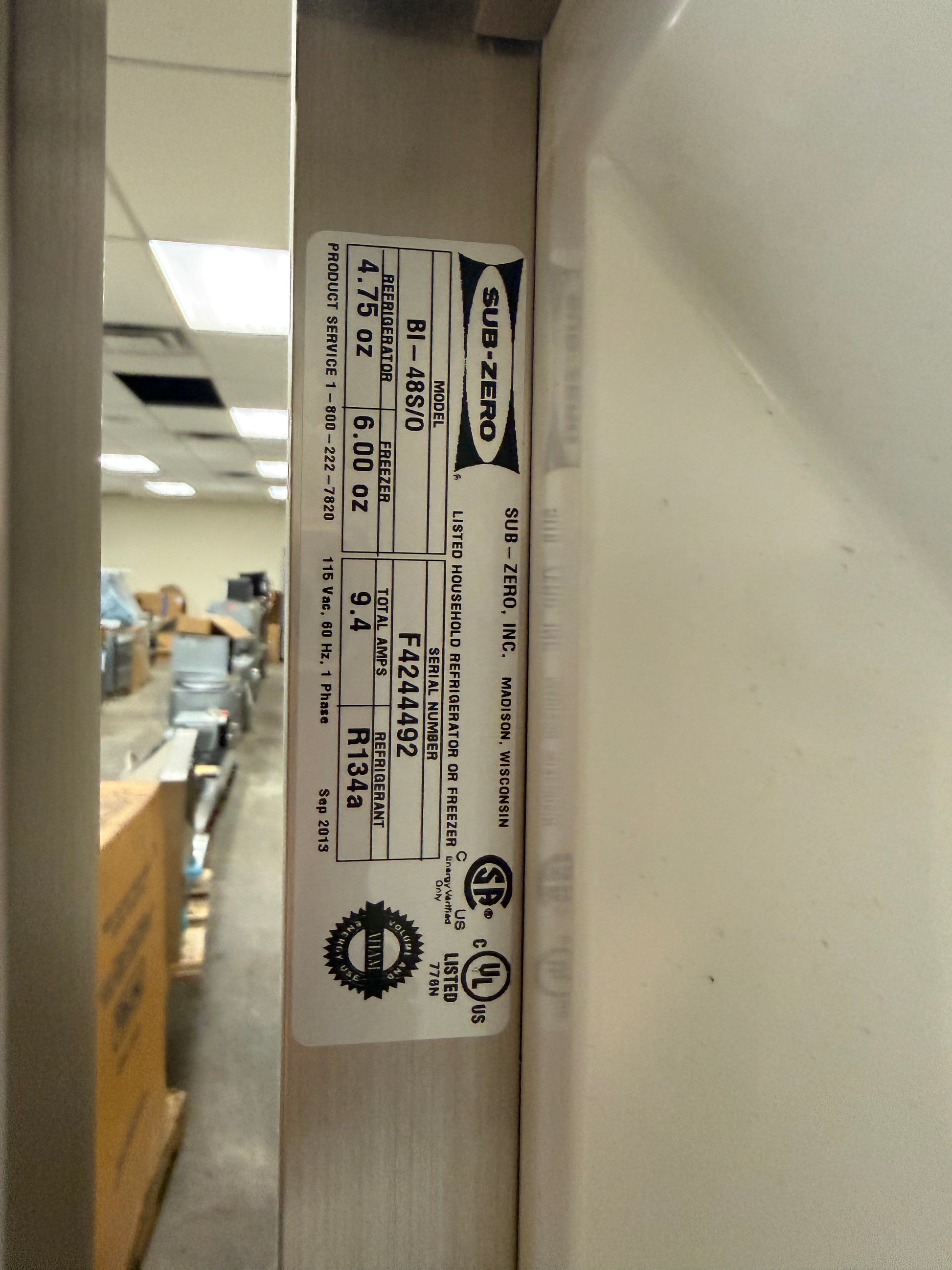 A close-up of a white appliance door edge showing a printed product label with model information and certification marks. The label includes the brand name SUB-ZERO and product code 81-858/0.