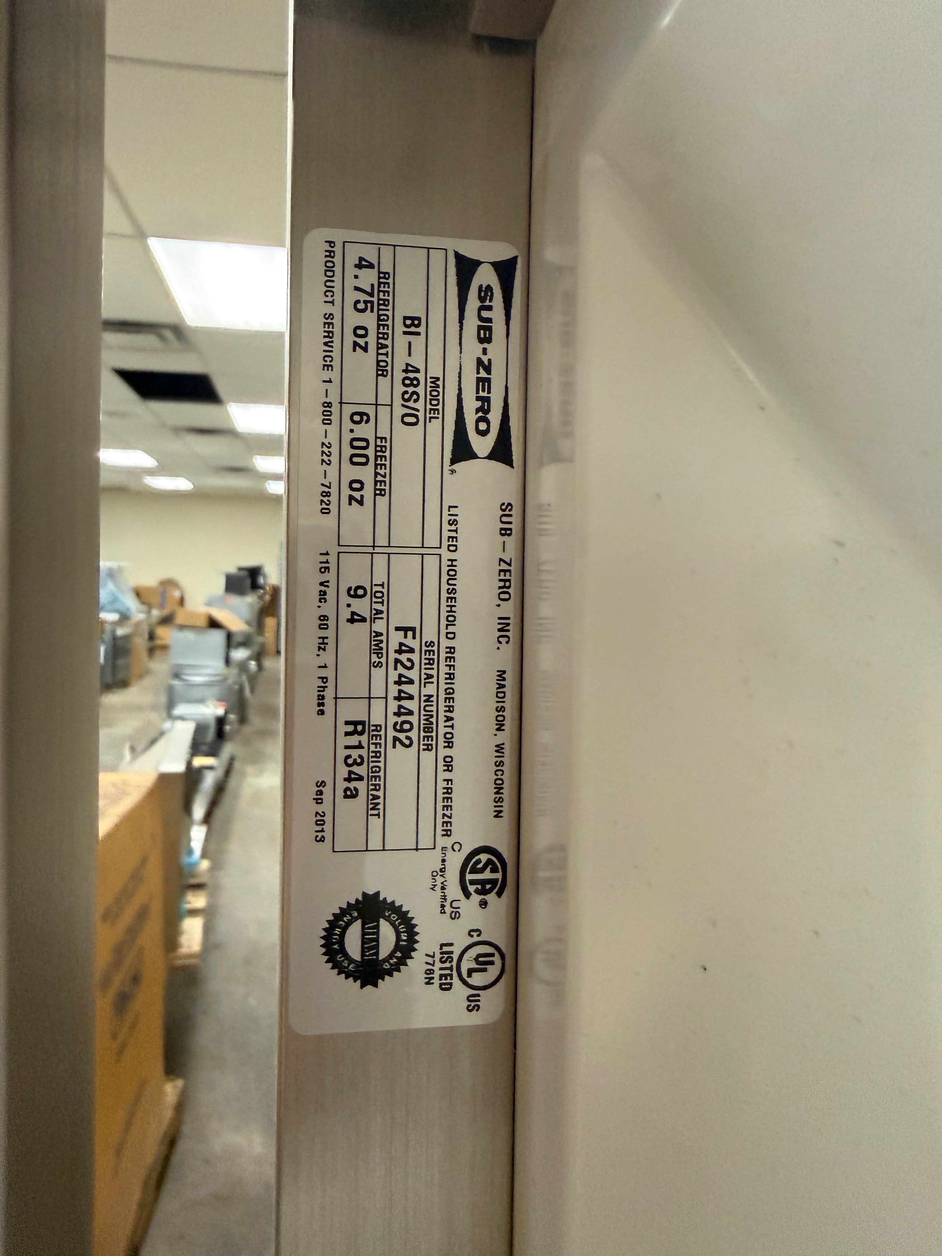 A close-up of a white appliance door edge showing a printed product label with model information and certification marks. The label includes the brand name SUB-ZERO and product code 81-858/0.