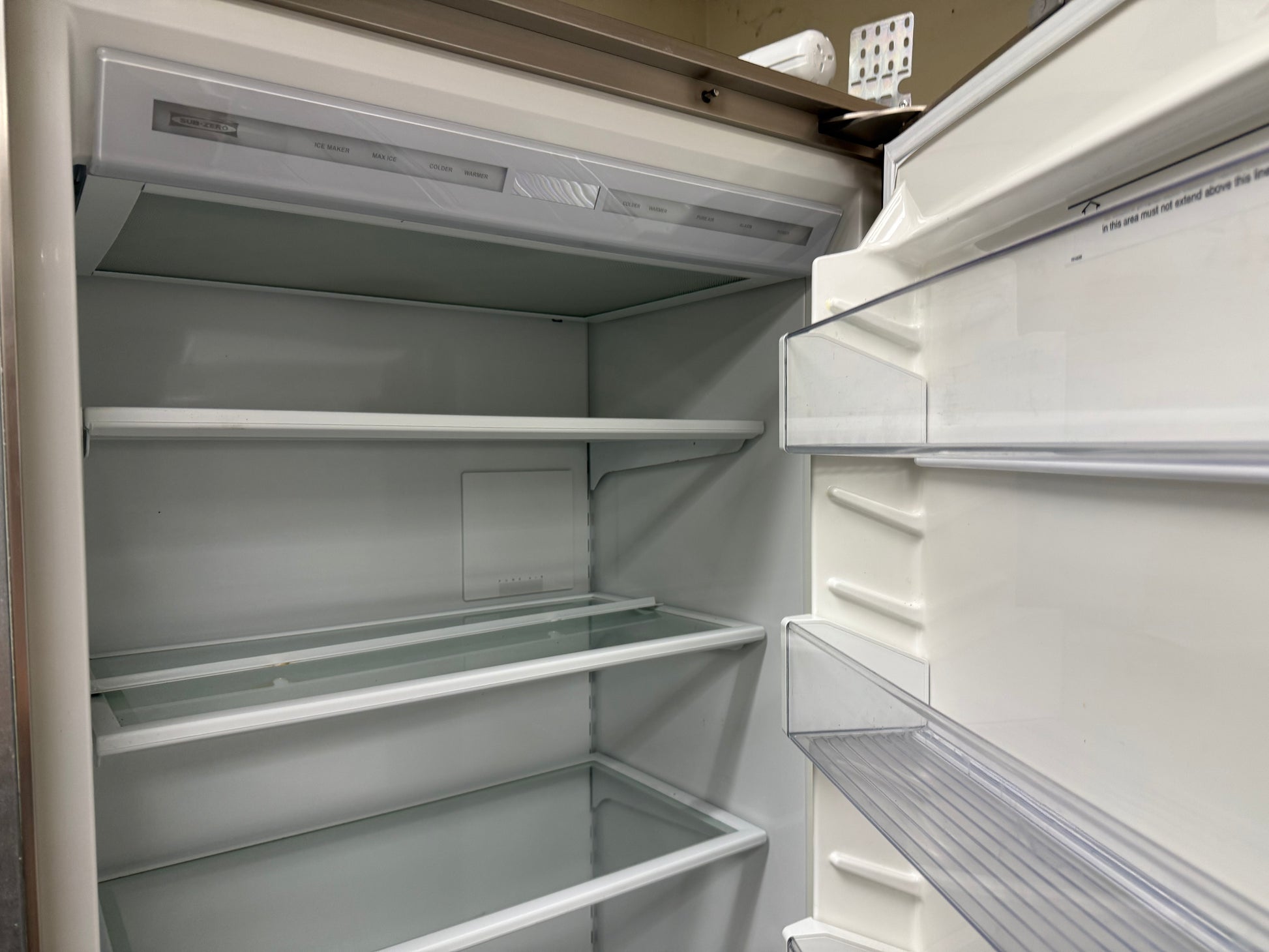 An empty white refrigerator shown from the open door perspective, with interior shelves, glass trays, and door storage compartments visible.