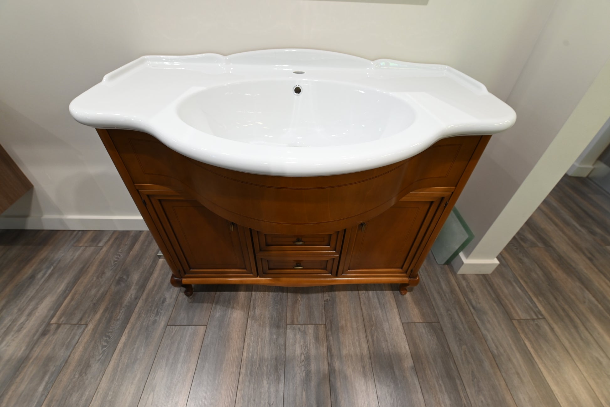 Wooden bathroom vanity with white sink on a wooden floor.
