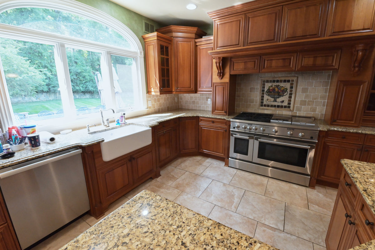 Aurora Circ traditional wood kitchen with raised panel cabinets farmhouse sink stainless range granite island and tiled backsplash