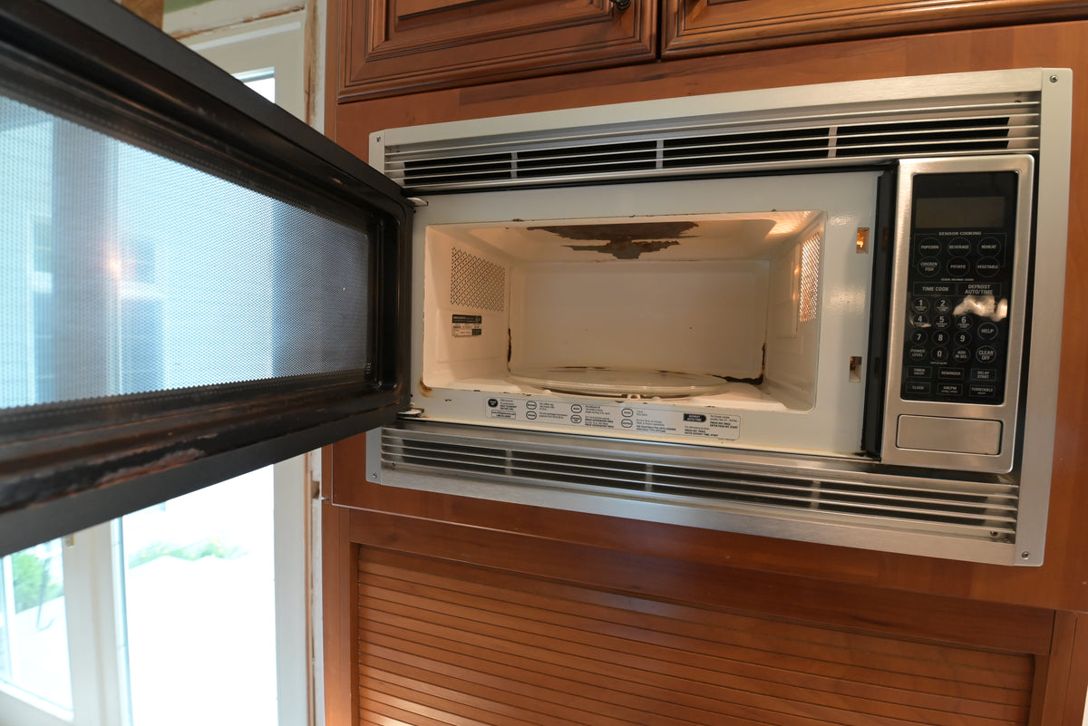 Aurora Circ built in microwave with open door set into traditional dark wood kitchen cabinetry showing a worn interior surface