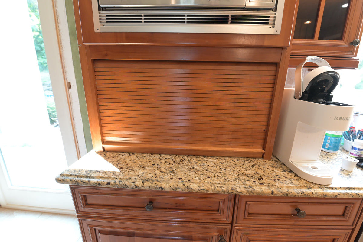 Aurora Circ traditional wood kitchen cabinetry with a slatted panel and granite countertop beside a compact coffee maker