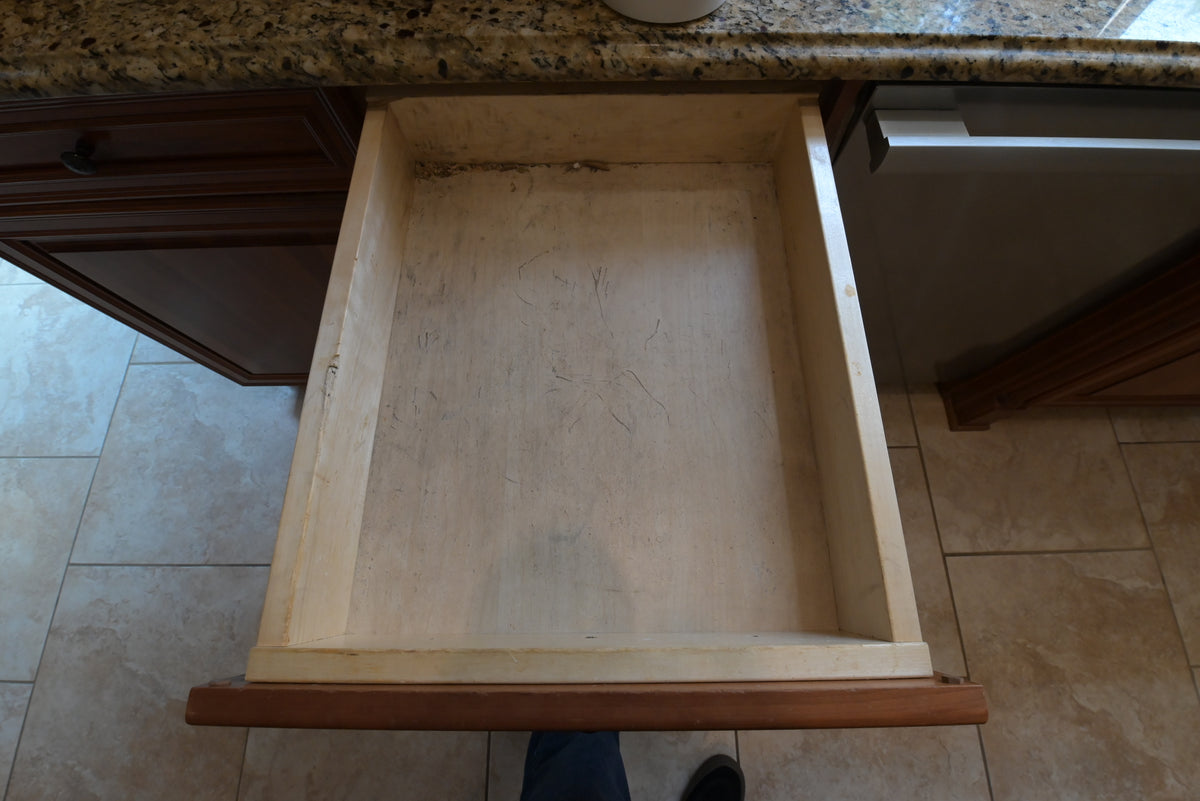 Aurora Circ traditional wooden kitchen drawer open beneath a speckled granite countertop with surrounding dark cabinetry
