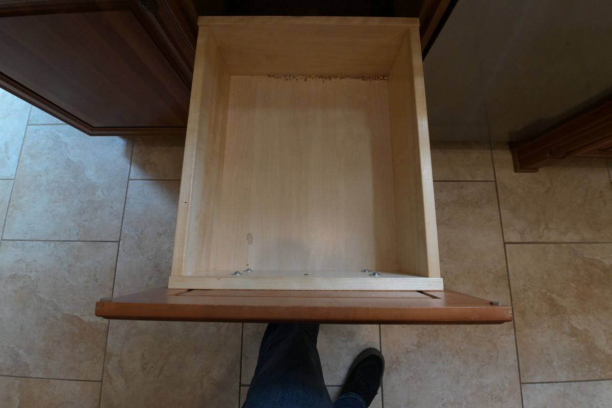 Aurora Circ traditional wooden kitchen cabinet drawer opened to reveal a spacious natural wood interior above tiled flooring
