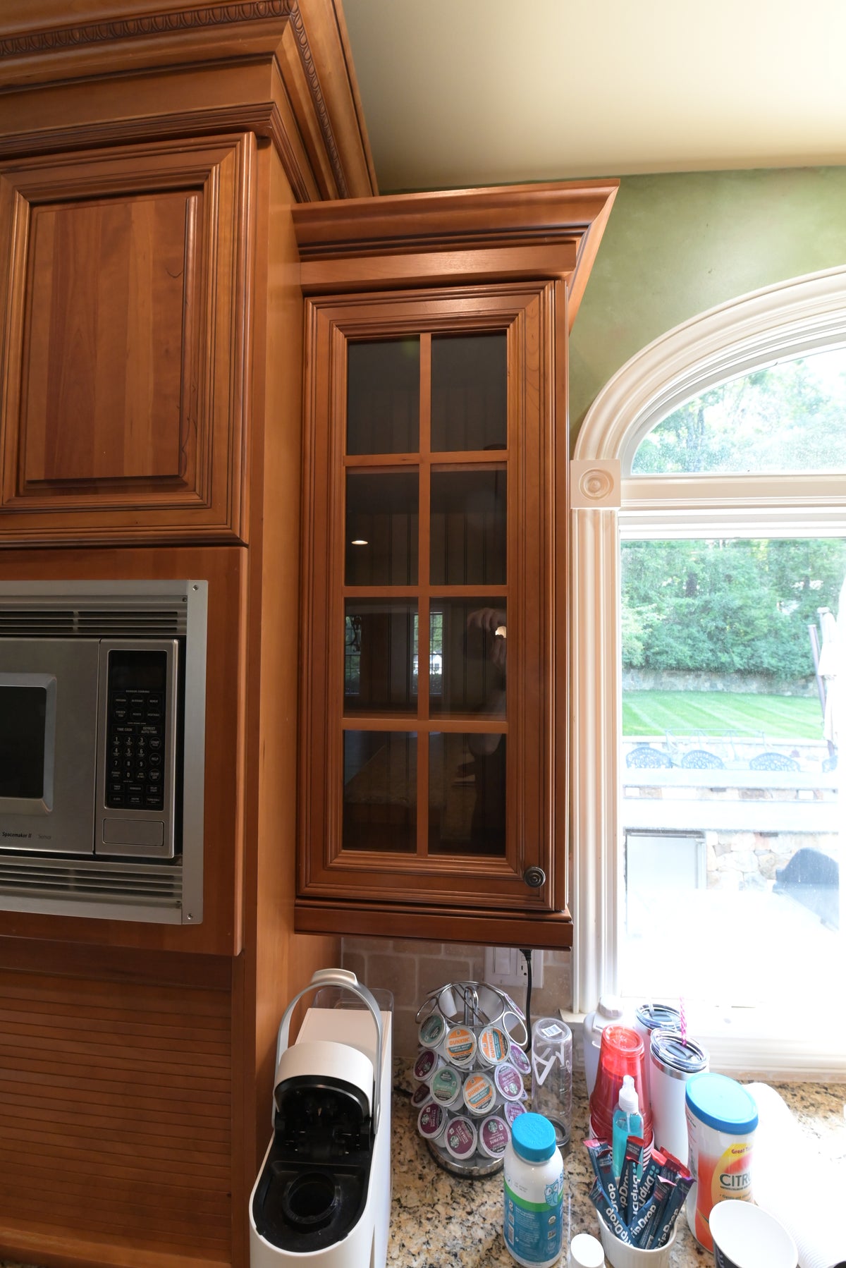 Aurora Circ traditional wooden kitchen cabinetry with glass door storage microwave and granite countertop beside an arched window