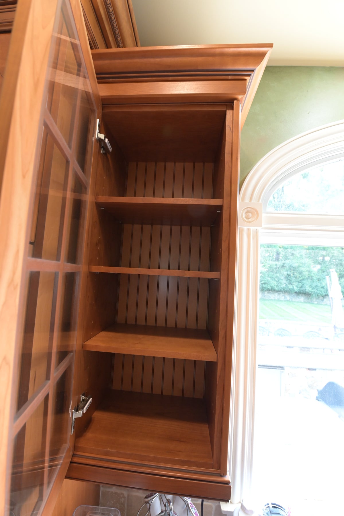 Aurora Circ traditional stained wood kitchen cabinet with open shelves and detailed crown molding beside an arched window
