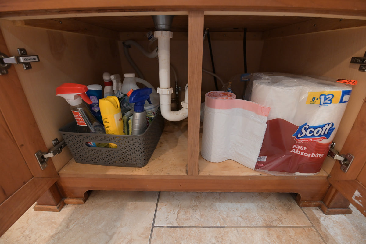 Aurora Circ traditional wood kitchen cabinet beneath a sink with cleaning supplies and paper towels stored inside