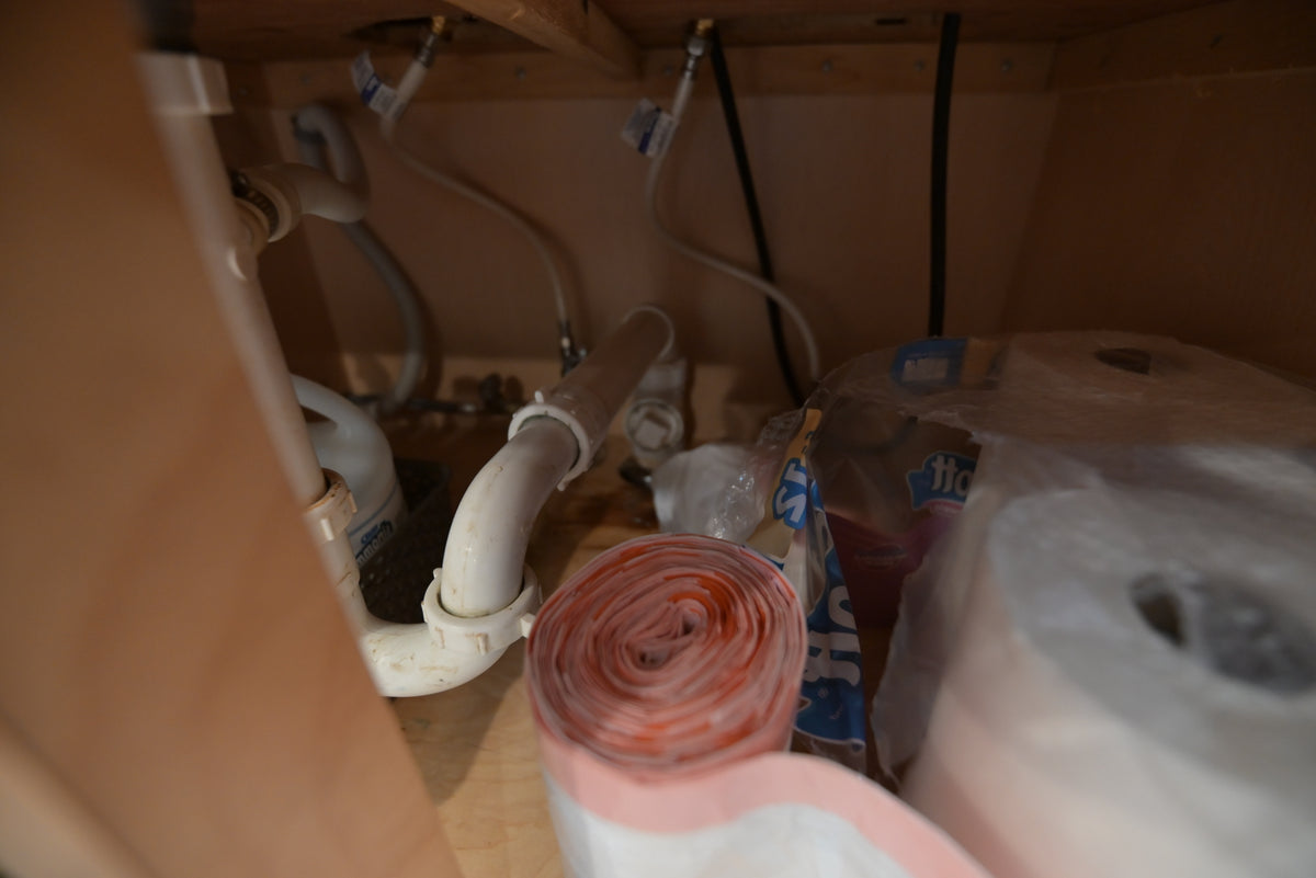 Aurora Circ kitchen cabinet interior with exposed sink plumbing and stored paper towel rolls beneath the countertop