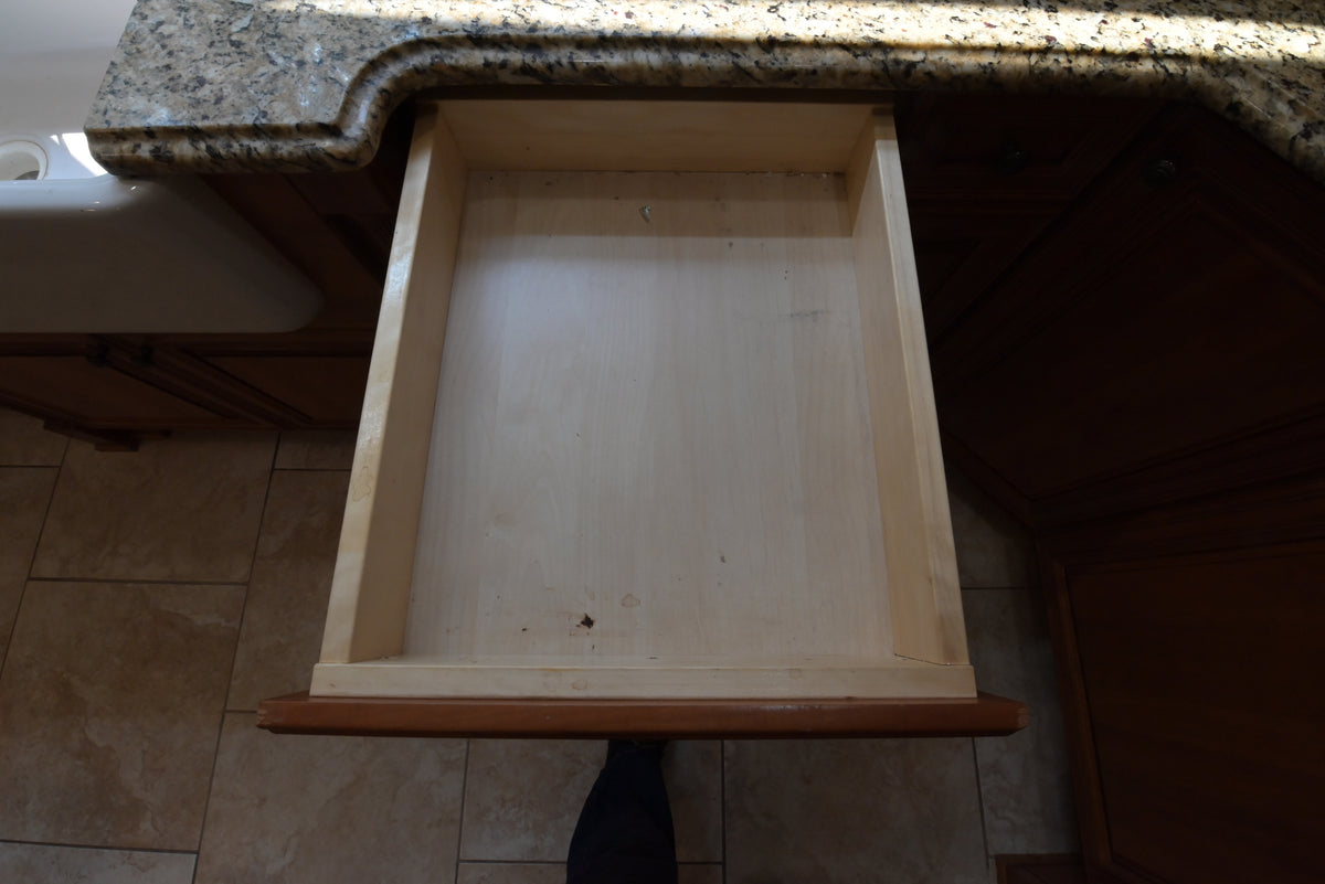 Aurora Circ traditional wooden kitchen drawer opened beneath a speckled granite countertop and classic cabinetry