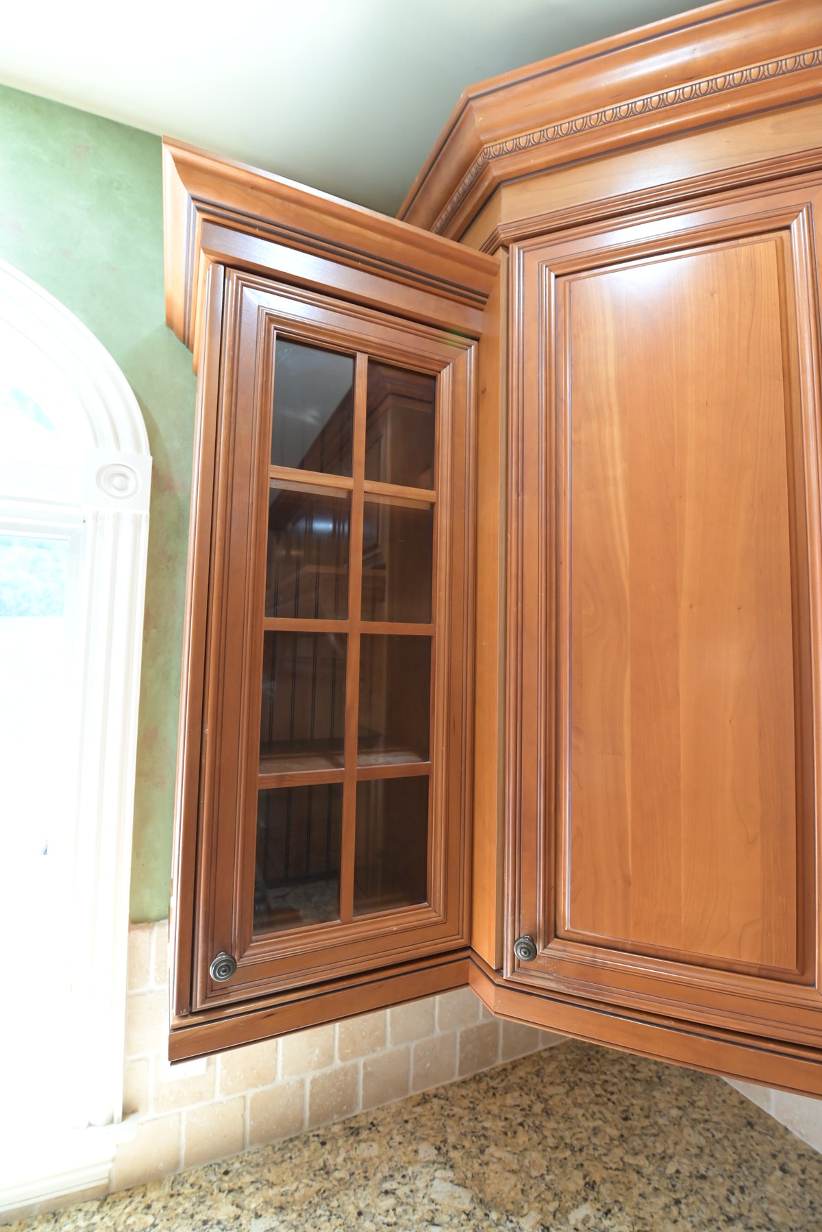 Aurora Circ traditional wooden kitchen cabinets with a glass front corner unit raised panels granite counter and brick backsplash