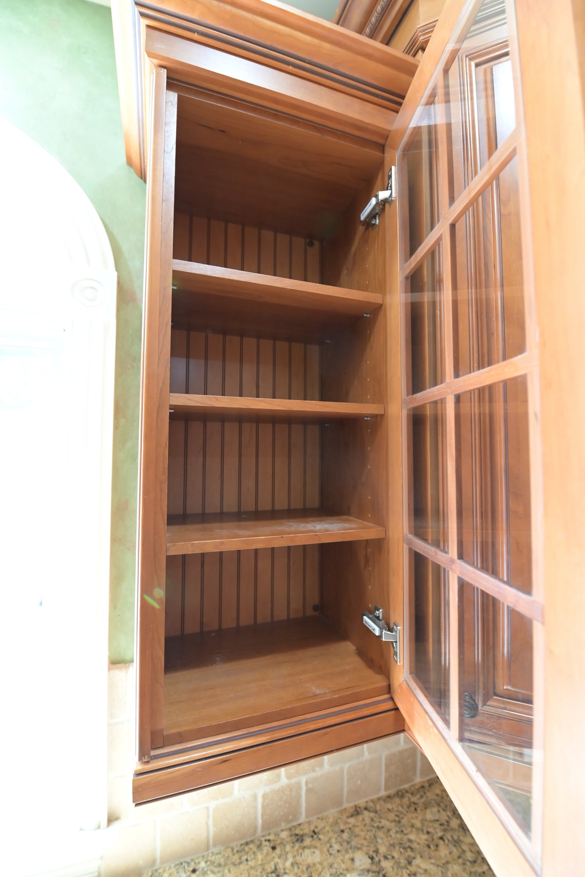 Aurora Circ traditional wooden kitchen cabinet with an open glass framed door and multiple interior shelves above a stone countertop