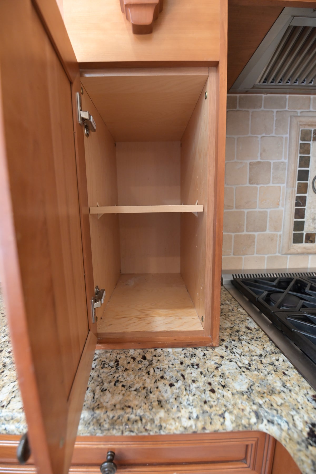 Aurora Circ traditional wood kitchen cabinet with open storage shelf above granite countertop beside a gas cooktop