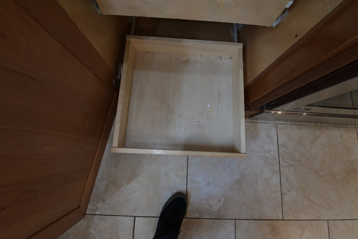 Aurora Circ traditional wooden kitchen cabinet with an open light wood drawer above beige tiled flooring