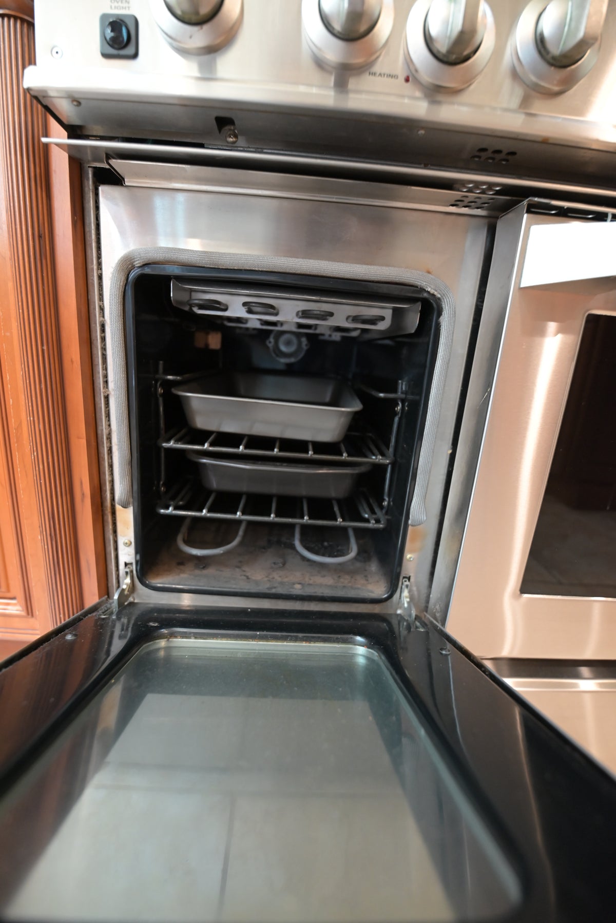 Aurora Circ stainless steel oven open to reveal multiple racks and baking trays within traditional wooden kitchen cabinetry
