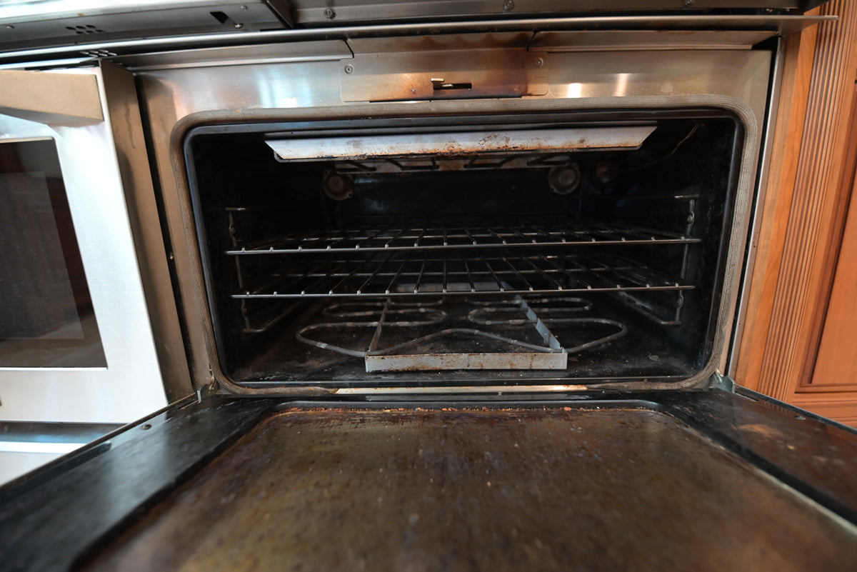 Aurora Circ stainless steel oven open to reveal interior racks and a well-used baking tray beside wood cabinetry