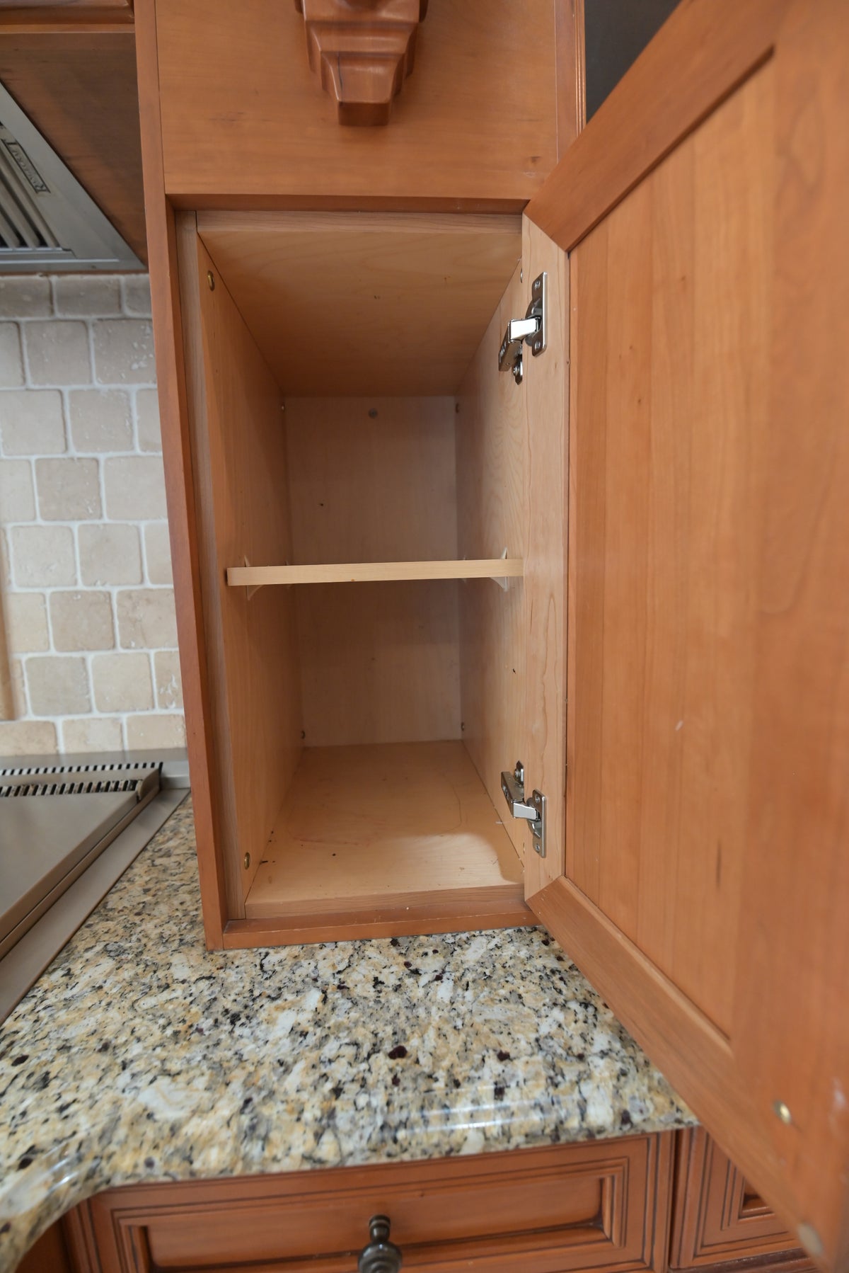 Aurora Circ traditional wooden kitchen cabinet with open interior shelf above a speckled granite countertop
