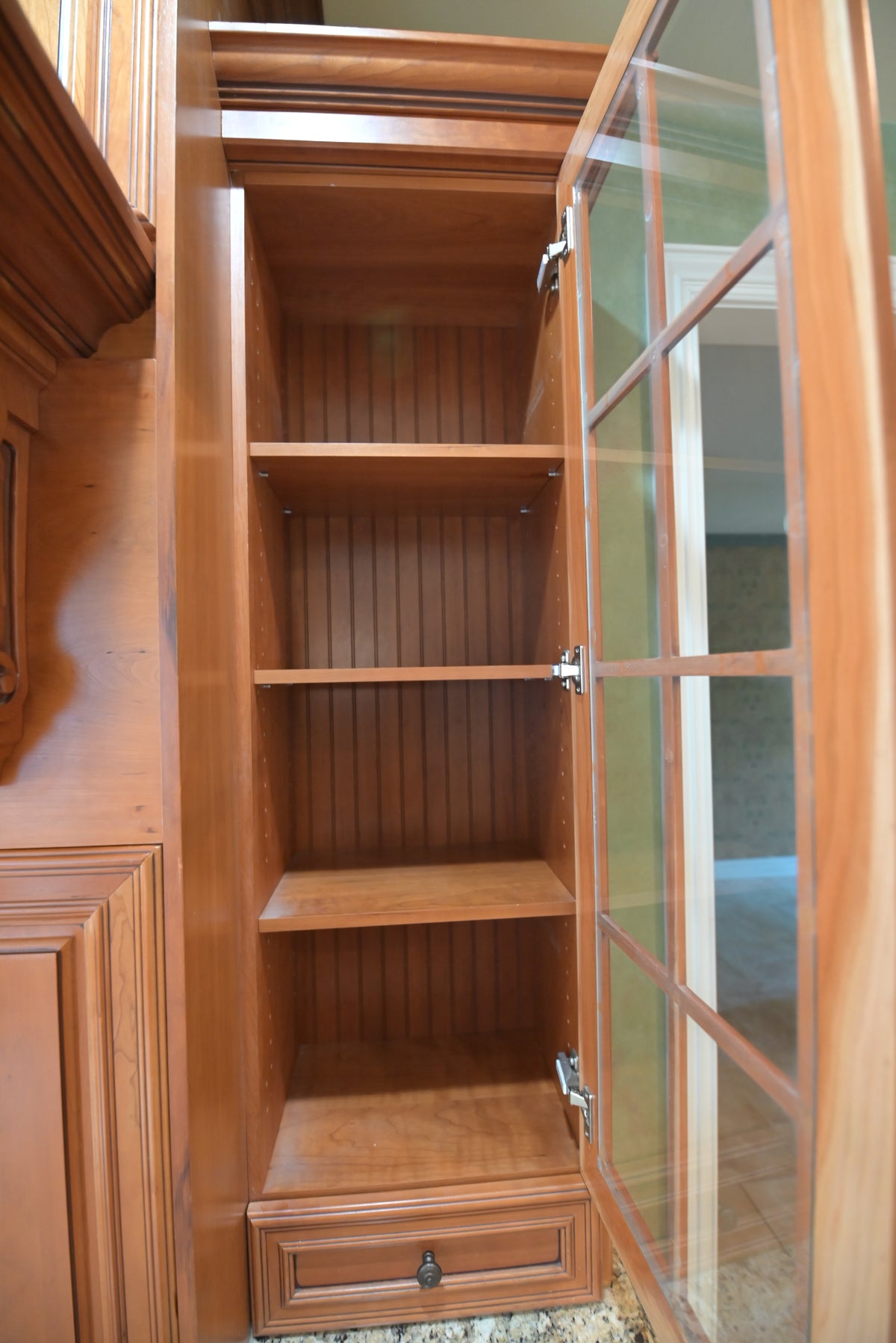 Aurora Circ traditional warm wood kitchen cabinet with glass door open to reveal two shelves beadboard backing and a bottom drawer