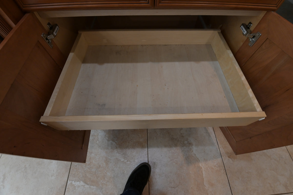 Aurora Circ traditional wooden kitchen cabinet drawer opened to reveal an empty light wood interior with visible hinges above tiled flooring