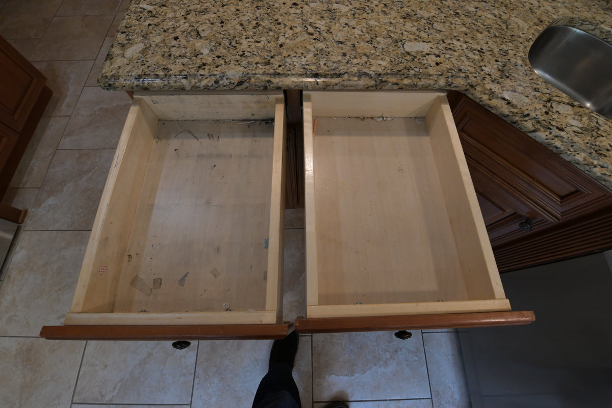 Aurora Circ traditional wooden kitchen cabinetry with two open drawers beneath a speckled granite countertop and sink