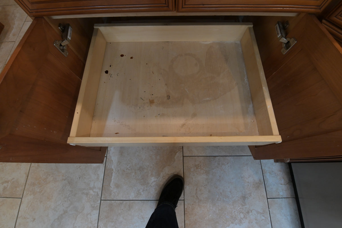 Aurora Circ traditional wooden kitchen drawer open to reveal a worn interior above tiled flooring