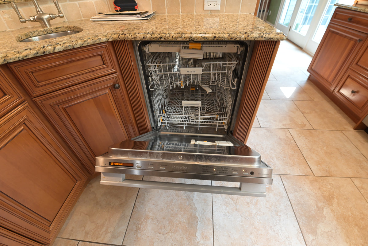 Aurora Circ traditional wood kitchen cabinetry with an open stainless steel dishwasher beneath a granite countertop
