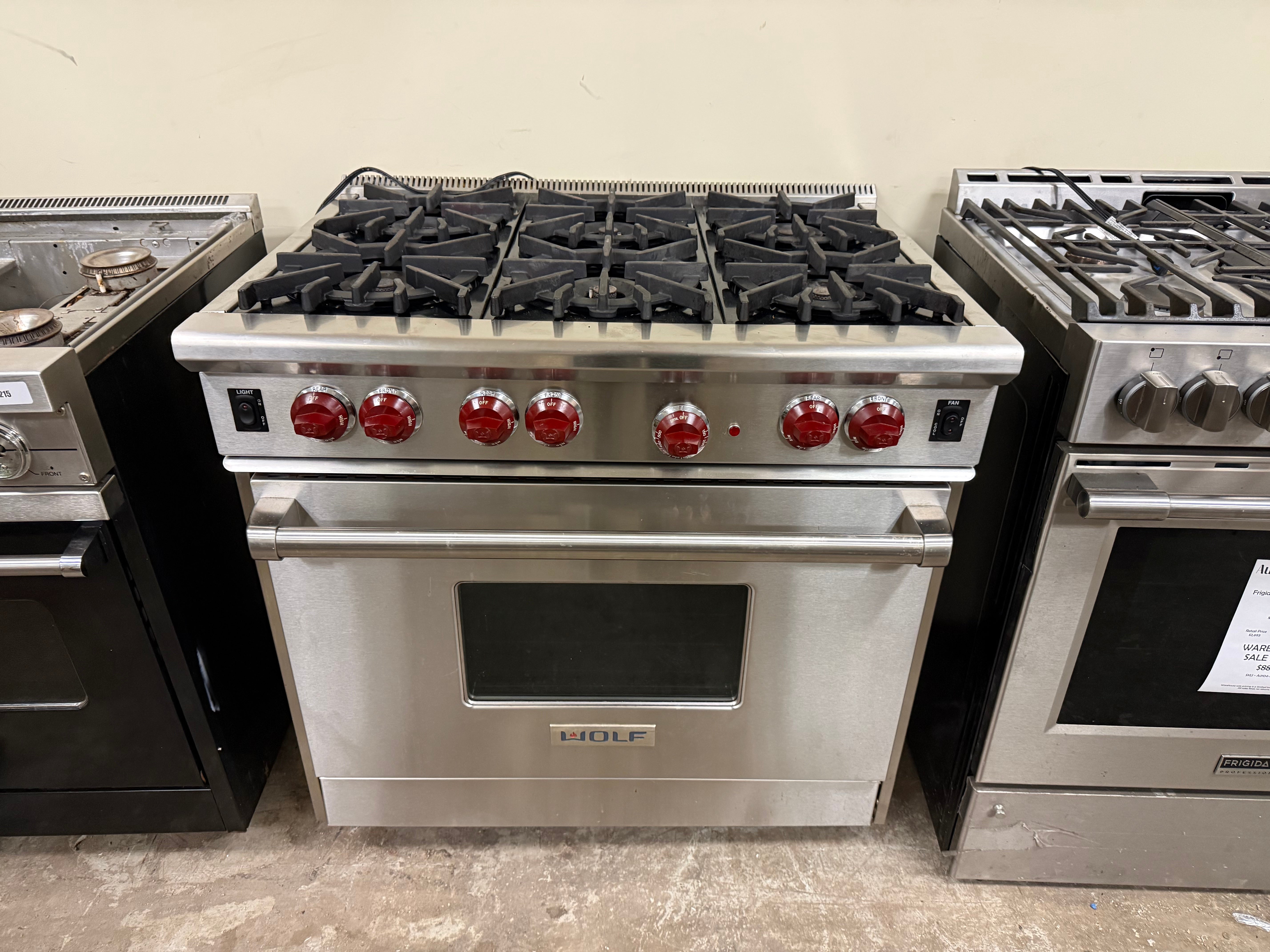 Stainless steel gas range with red knobs on a concrete floor.