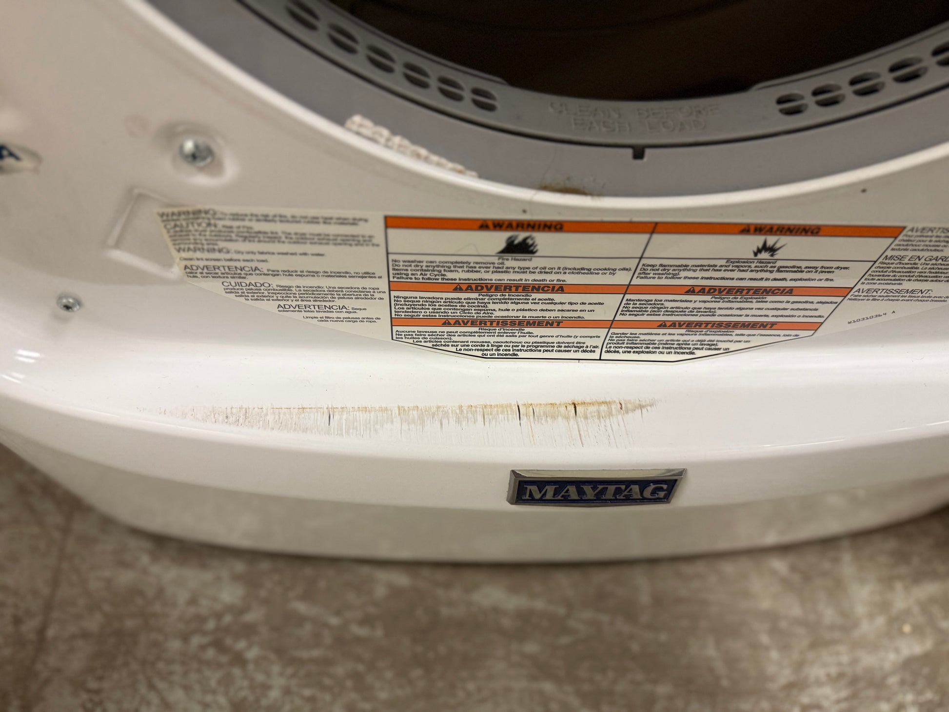 White appliance with Maytag logo and warning labels on a gray floor.