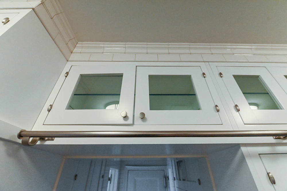 White cabinet with glass doors and silver handles in a kitchen setting.