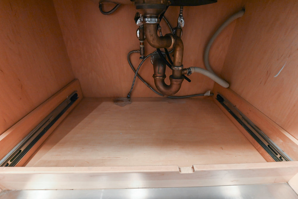 Under-sink plumbing setup with wooden cabinet and metal components.