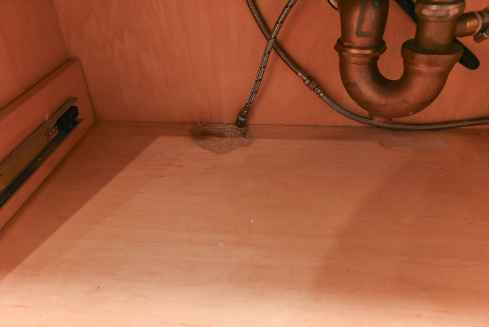 Close-up of a kitchen sink area with pipes and a drain.