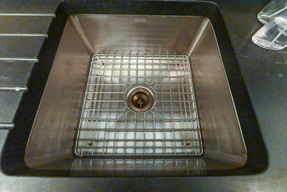 Stainless steel kitchen sink with grid drain on a black countertop
