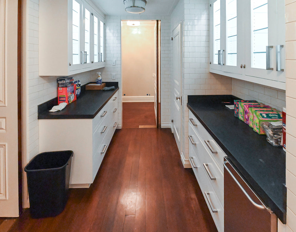 Modern kitchen with white cabinets, black countertops, and wooden flooring.