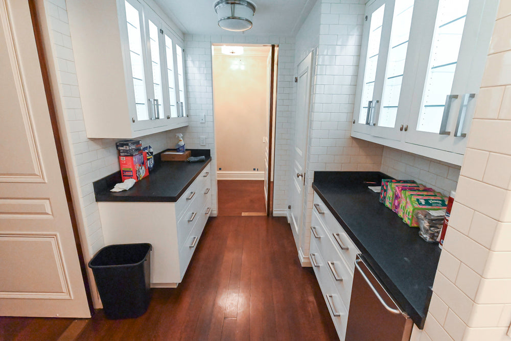 Pre-owned dry bar with white cabinets, black countertops, and wooden flooring.