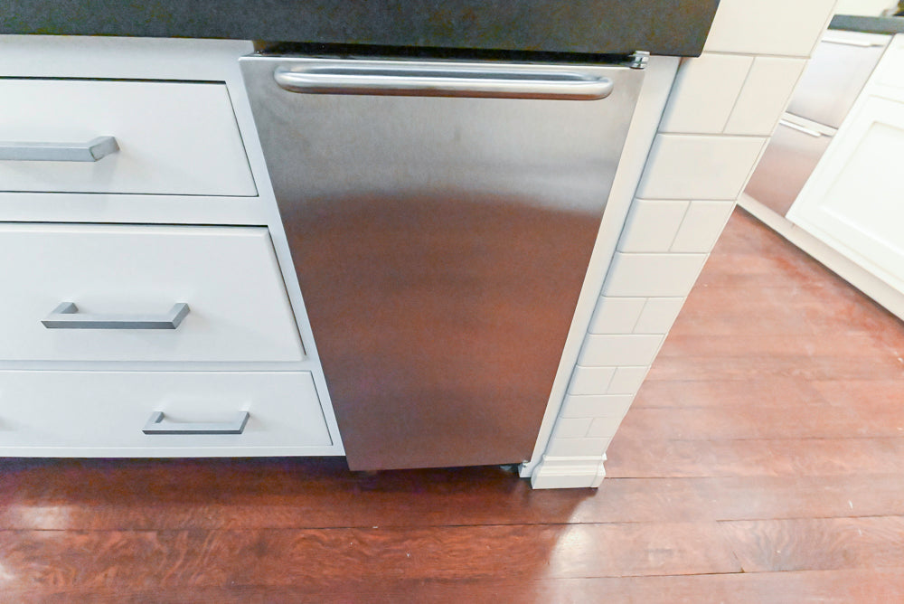 Stainless steel dishwasher in a kitchen with white cabinets and wooden floor.