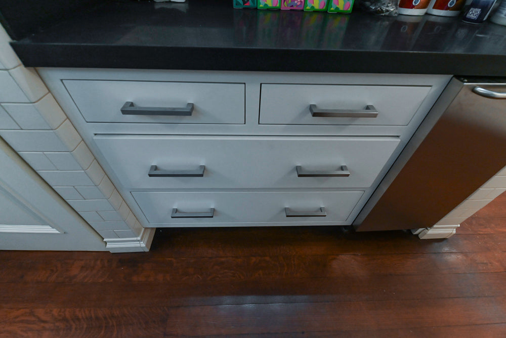 White kitchen cabinet with multiple drawers and a dark countertop.