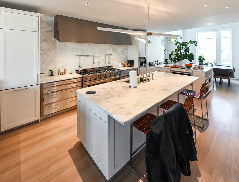 Modern kitchen with white island, stainless steel appliances, and wooden flooring.