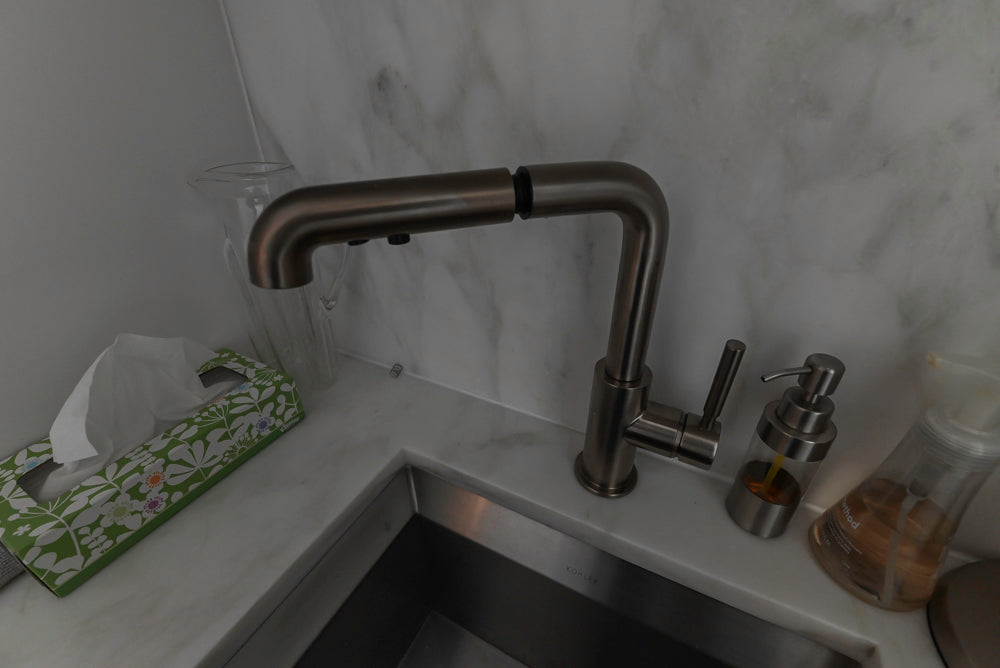Modern kitchen faucet on a marble countertop with various items.