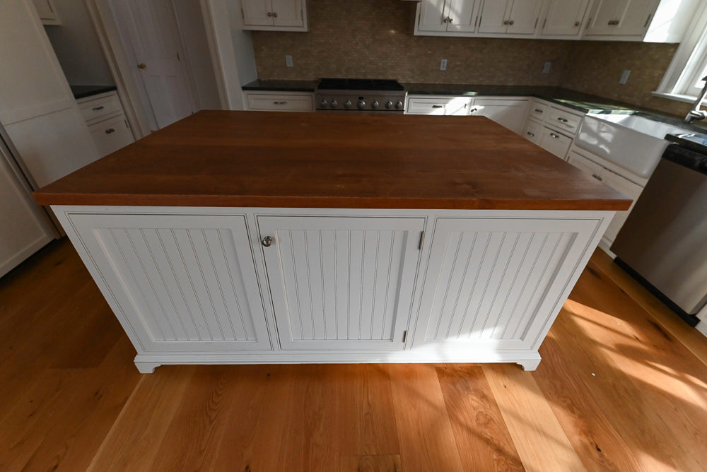 Kitchen island with wooden top and white base cabinets in a well-lit kitchen.