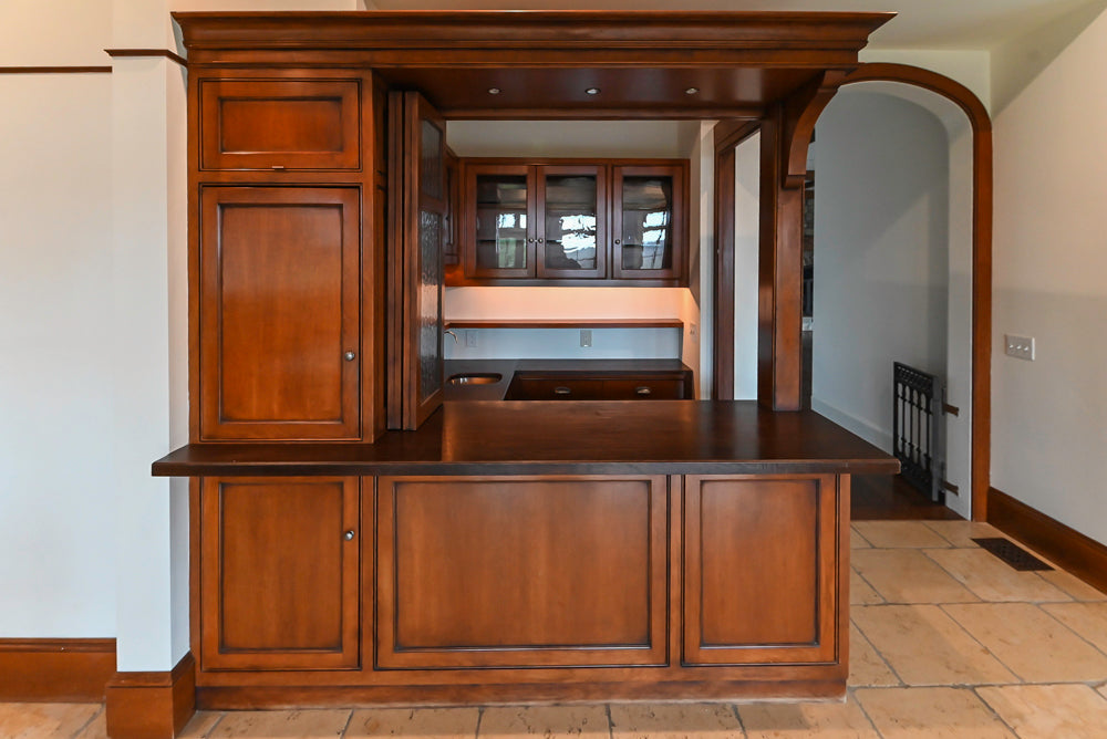 Luxury wooden bar area with raised panel cabinets and bar faucet