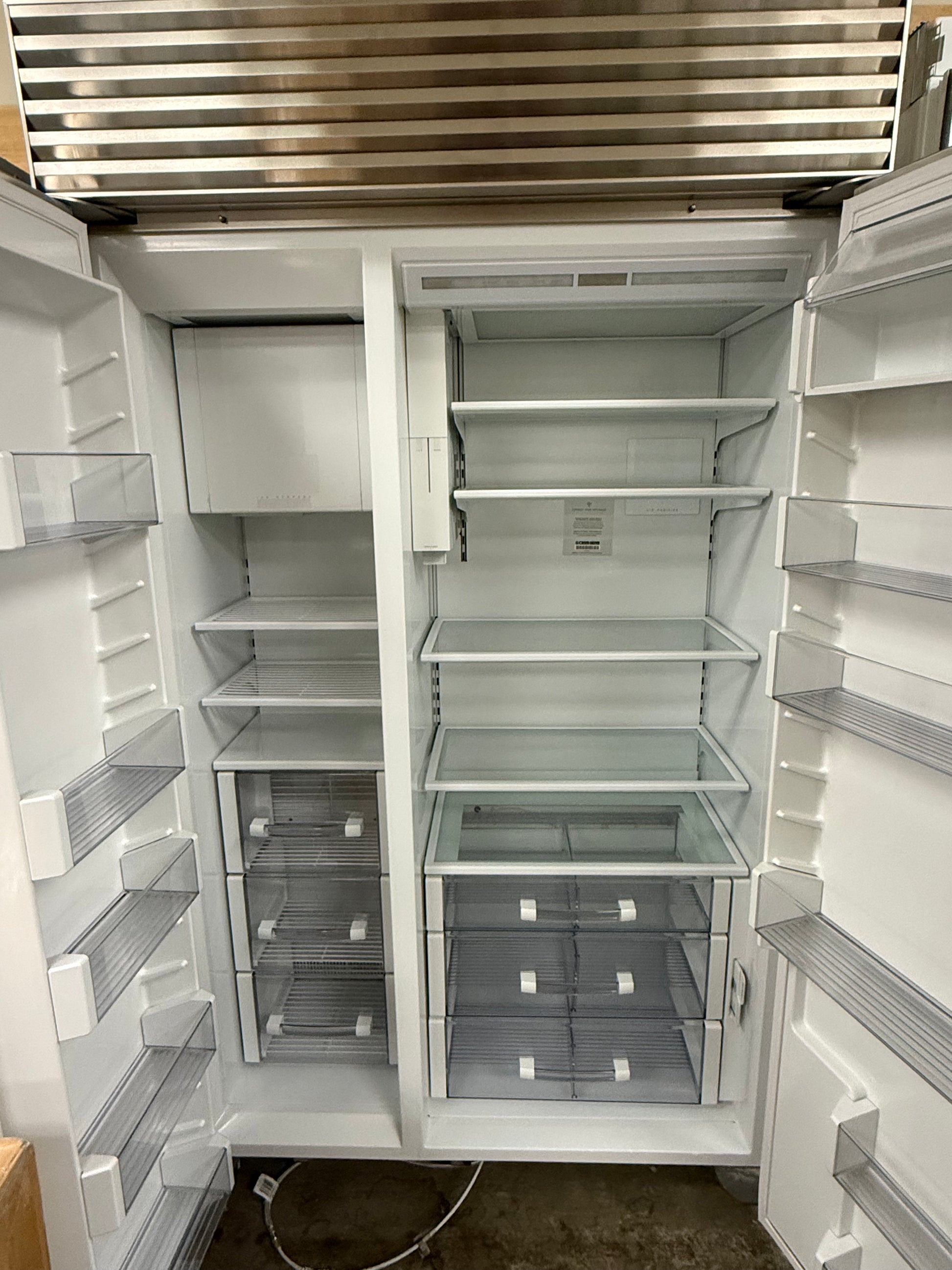 Pre owned Sub Zero 48 inch built in refrigerator open doors showing separate refrigerator and freezer compartments with bright LED lighting