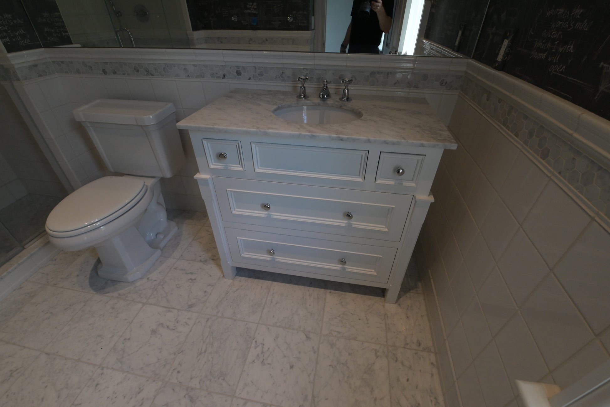 A light blue vanity cabinet with a white marble-look countertop and an undermount sink, shown in a tiled bathroom next to a white toilet.