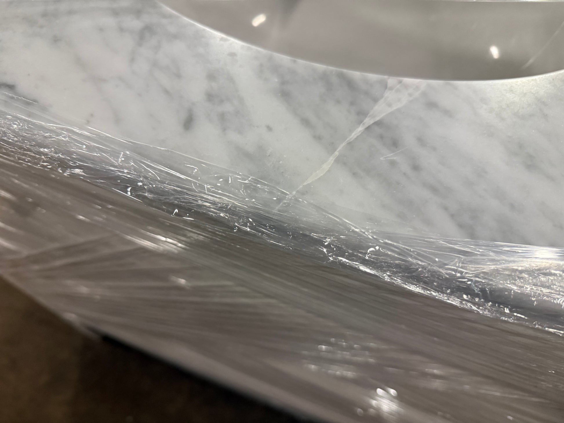 Close-up of a white and gray marble-look surface wrapped in clear plastic, with part of a curved white basin or container visible at the top.