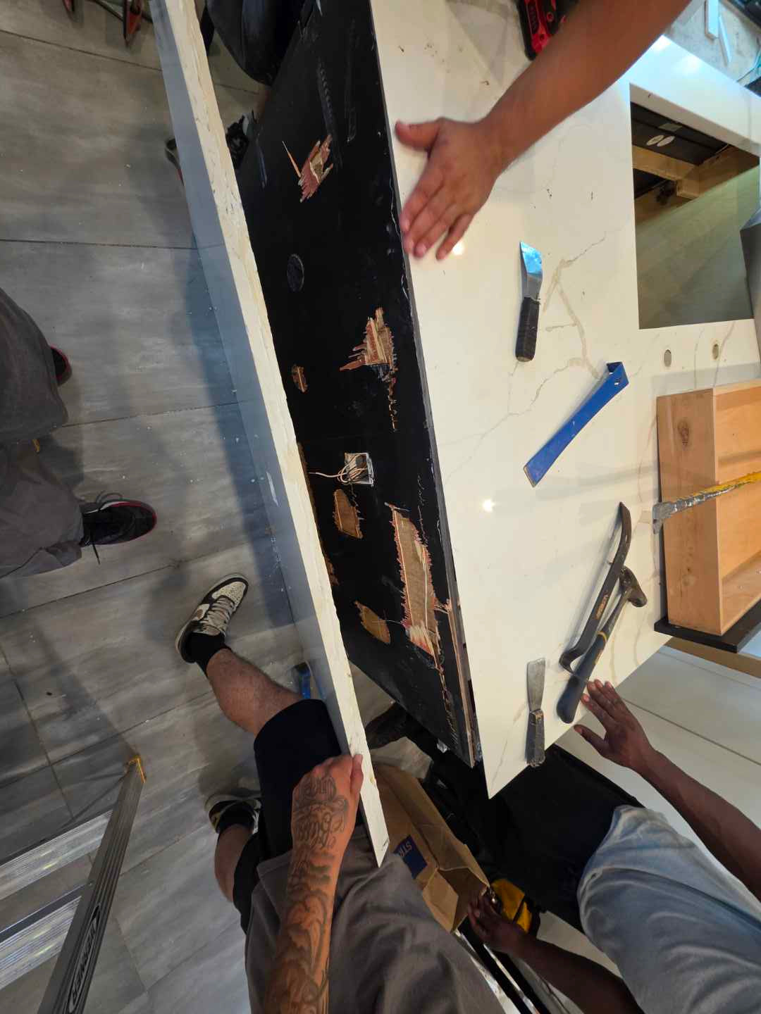 Aurora Circ white veined kitchen countertop being fitted by installers over dark cabinetry during installation